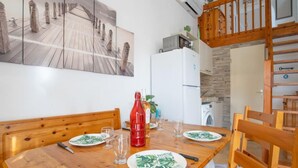 Ein Essbereich mit einem Holztisch, gedeckt für vier Personen, umgeben von Holzstühlen. Über dem Tisch hängt ein großes Gemälde an der Wand.
