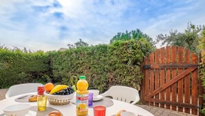 Ein Essplatz im Freien mit Frühstücksangeboten, darunter Croissants, Obst und Getränke, umgeben von Stühlen und einem Holztor.
