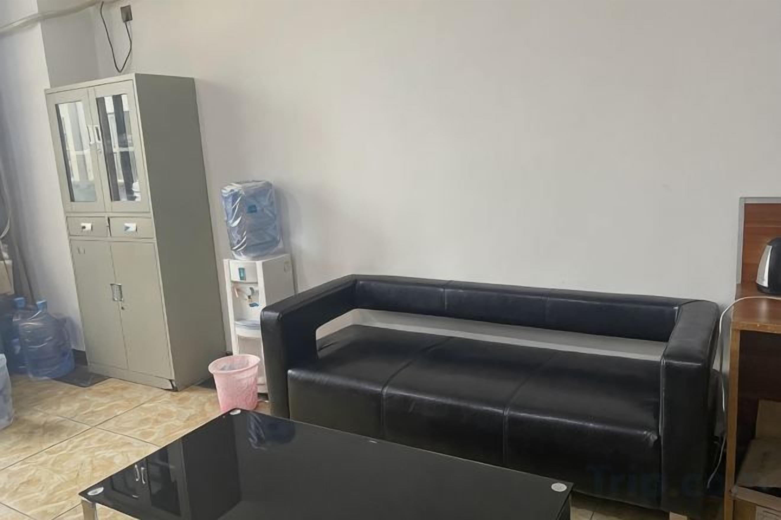 Una habitación con un sofá de cuero negro, una mesa de centro con tapa de vidrio, un mueble con puertas de cristal y un dispensador de agua.