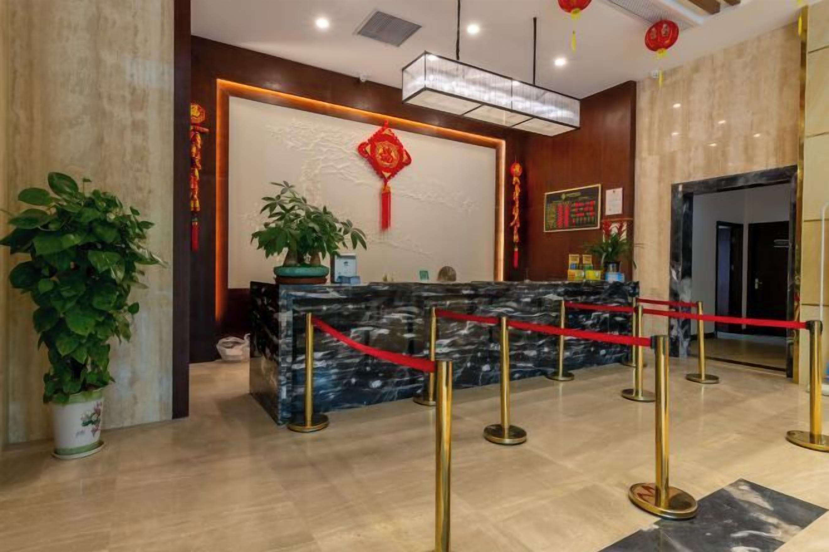 A hotel reception area with a marble counter, red ropes, and potted plants.