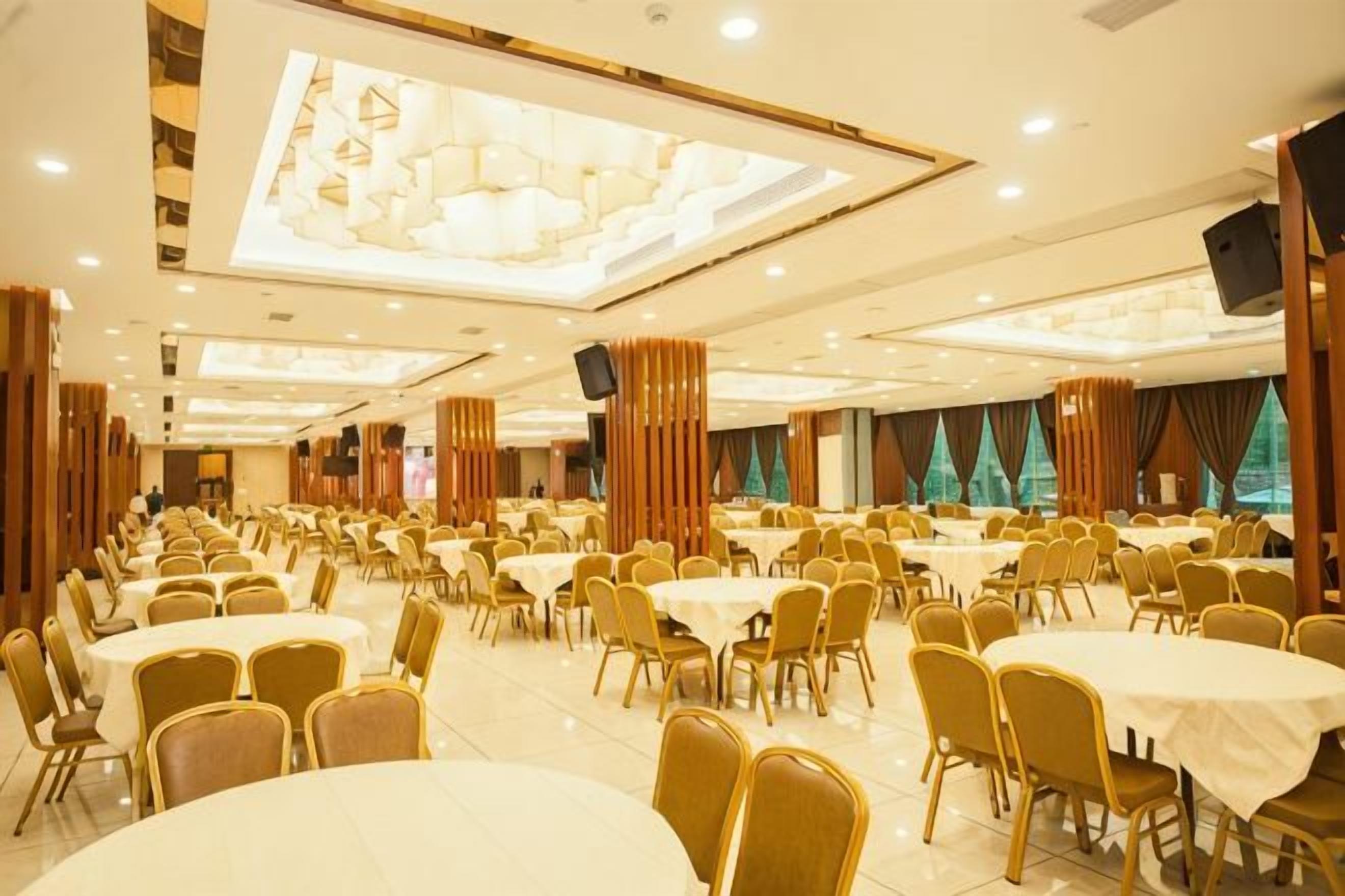 Una sala banchetti con numerosi tavoli rotondi e sedie, soffitti alti con lampadari e un grande schermo.