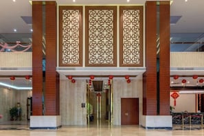 A hotel lobby with a reception desk, a large entrance, and a decorative wall with geometric patterns. - Wonderful Hotel (Huidong)