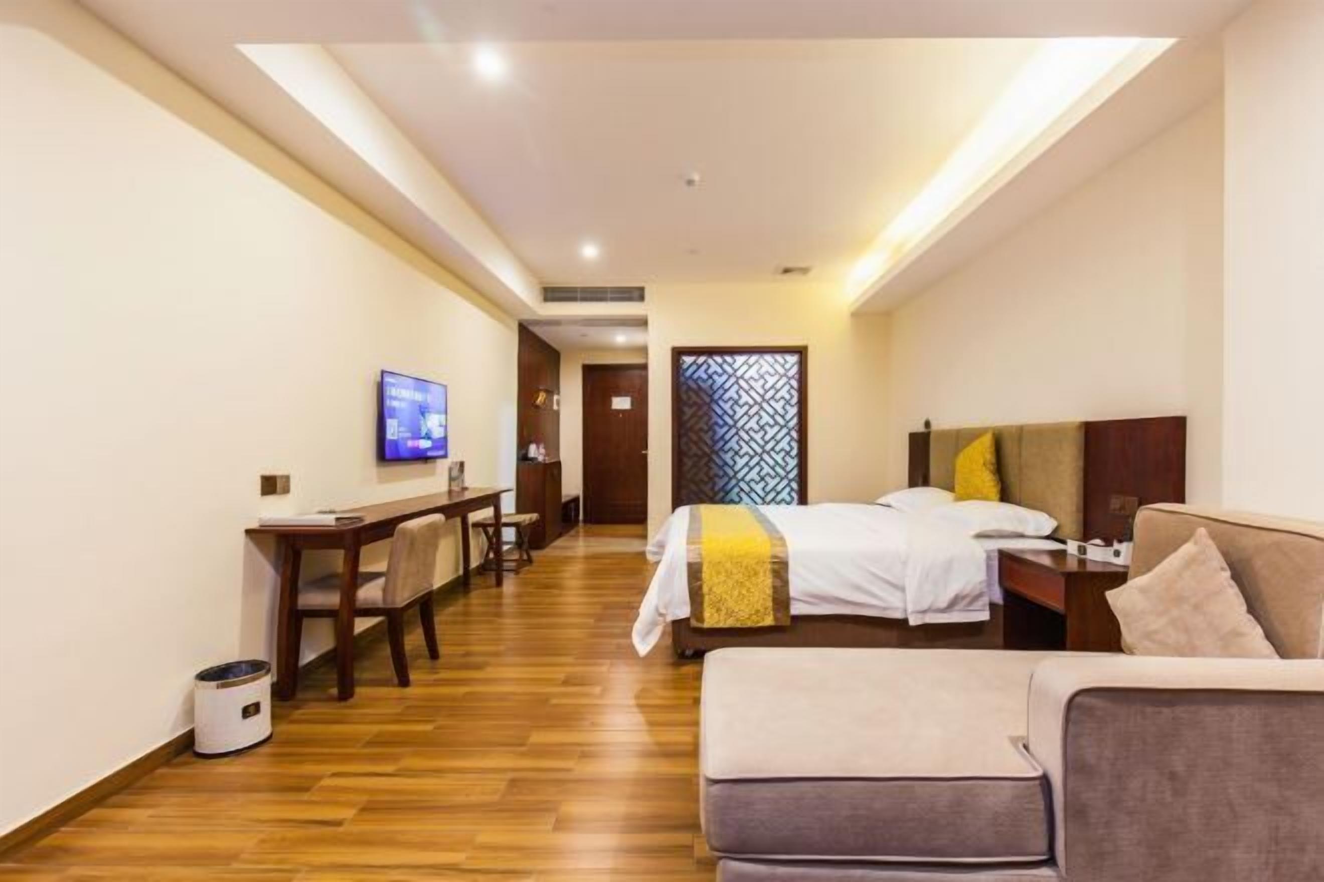 Quarto de hotel com cama, escrivaninha, televisão e sofá.