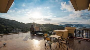 Una terraza de madera con mobiliario exterior, vista a montañas y cielo despejado.