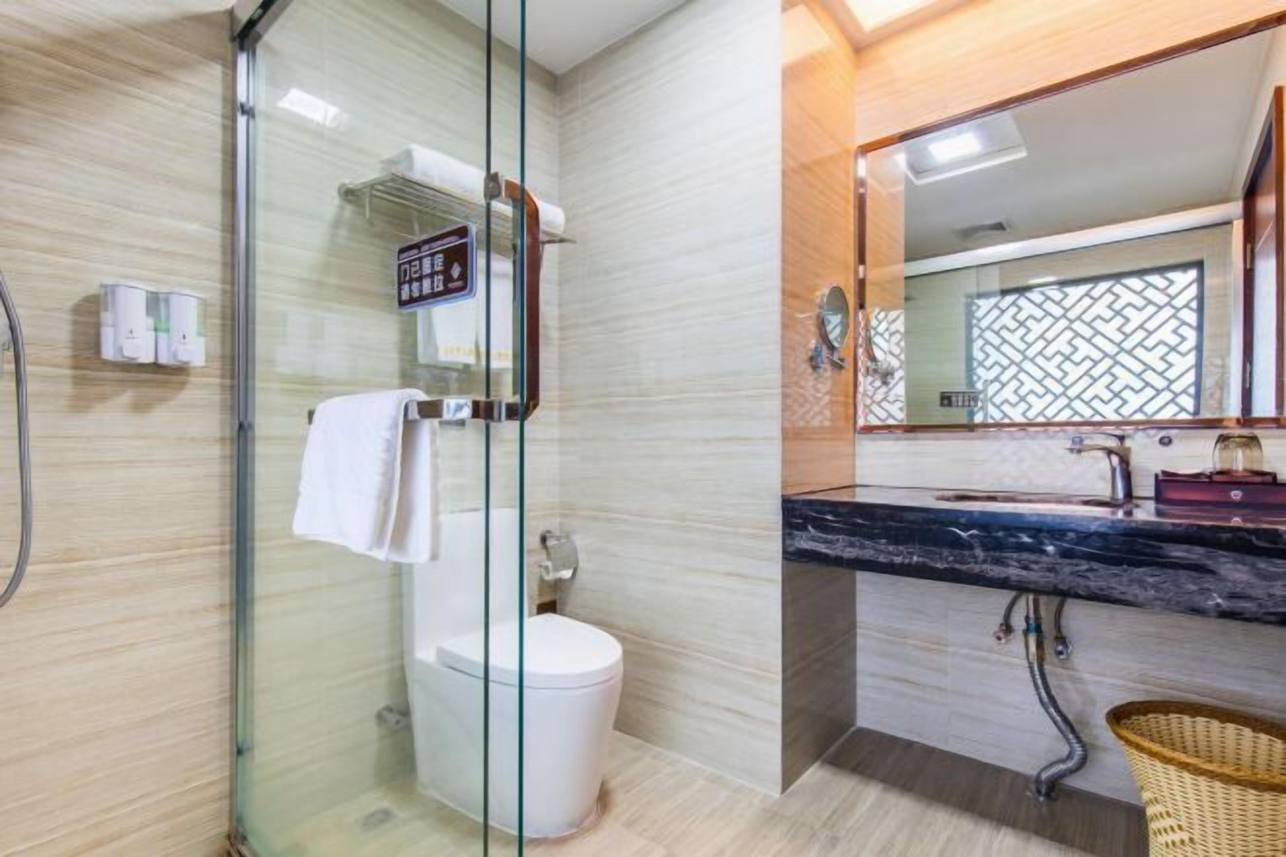 Um banheiro moderno com box de vidro, vaso sanitário branco, pia de mármore e espelho com detalhes geométricos no revestimento.