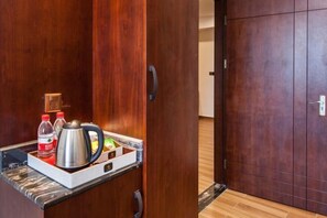 A hotel room with a wooden wardrobe, a tray with a kettle, bottles, and a box.