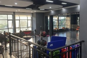 Un gimnasio con equipo de ejercicio, una colchoneta azul y vistas al exterior a través de amplios ventanales.