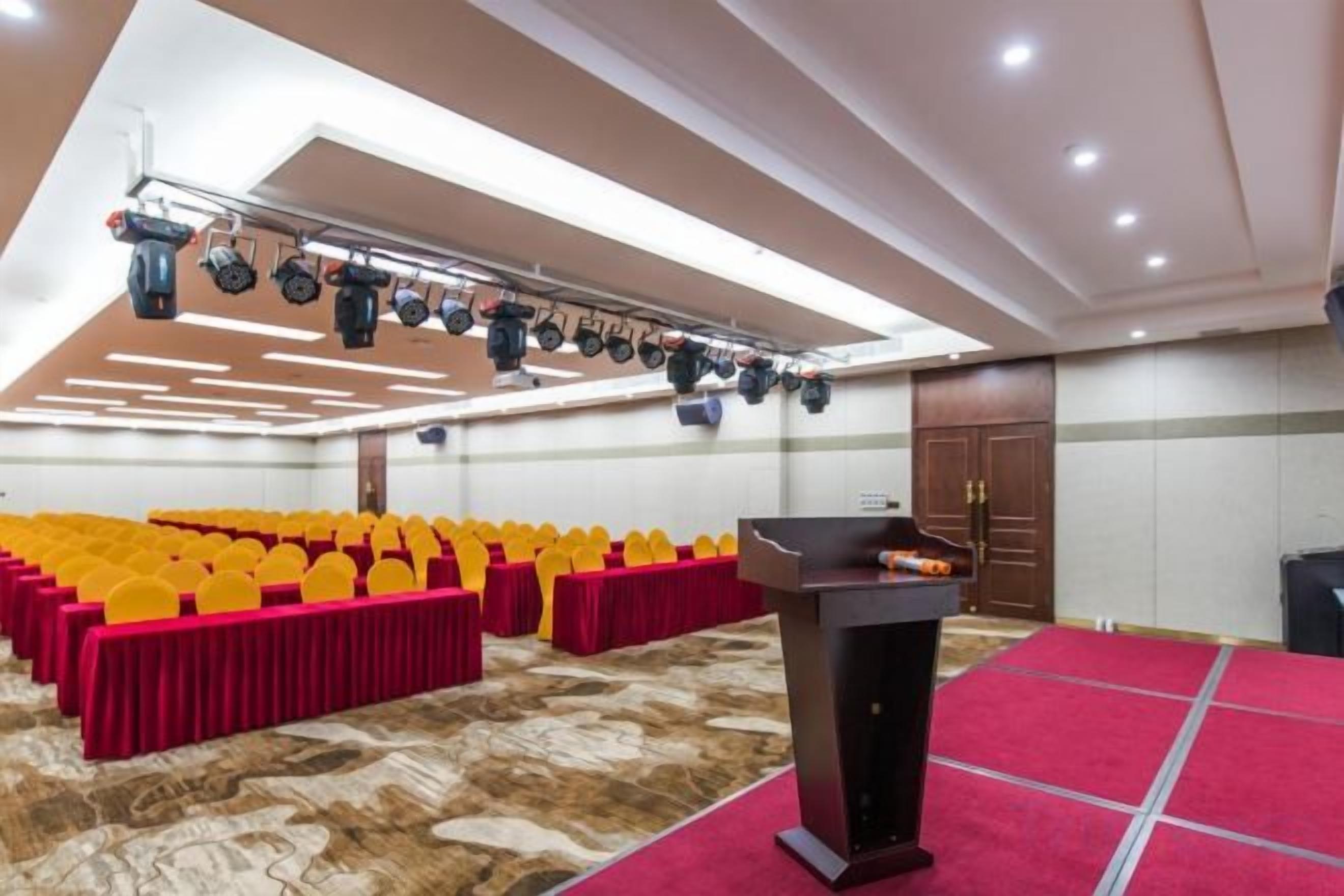 A conference room with rows of yellow chairs, a podium, and a carpeted floor.