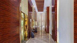 A hallway with wooden paneling, a marble floor, and a view into a room with a bed and a desk. - Wonderful Hotel (Huidong)