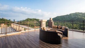 A rooftop terrace with a curved seating area, a railing, and a view of a hilly landscape. - Wonderful Hotel (Huidong)