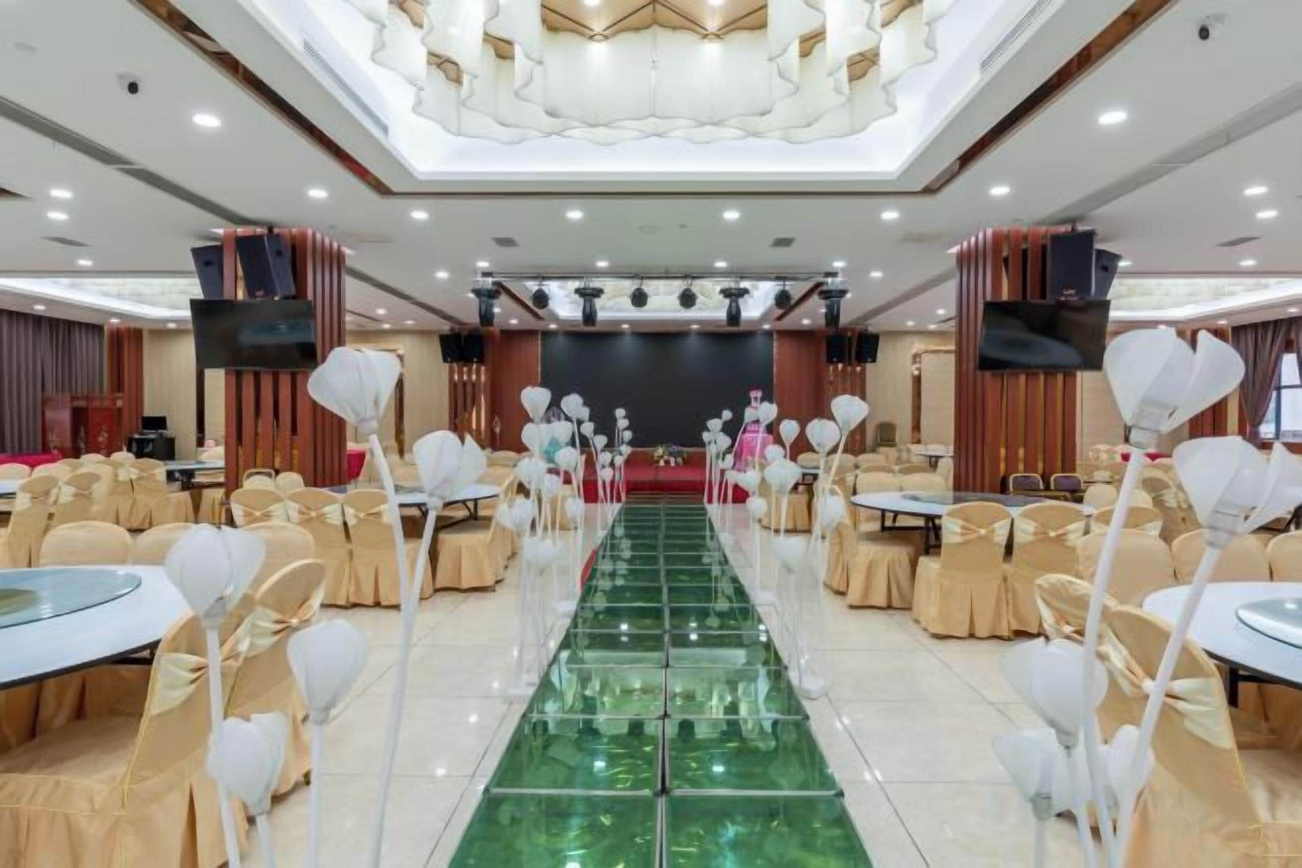 Un salón de banquetes con mesas redondas, un pasillo central y un escenario al frente.