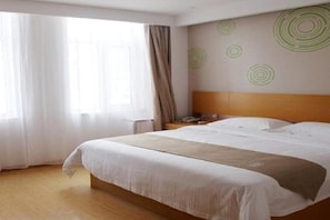 A hotel room with a large bed, a wooden headboard, a bedside table, and a window with sheer curtains.