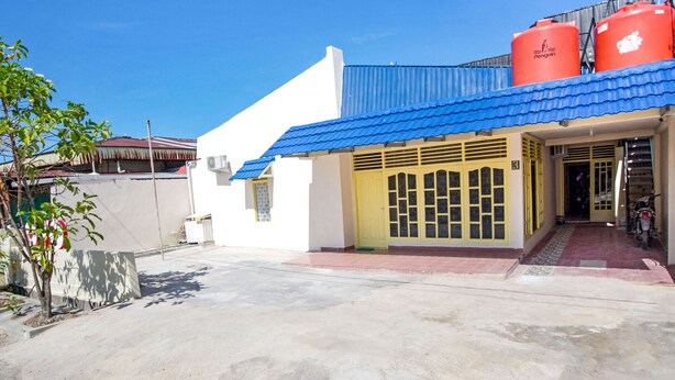 A building with a blue roof and a yellow door, featuring large red water tanks on the roof. - OYO 3252 Lansano Residence (Padang)
