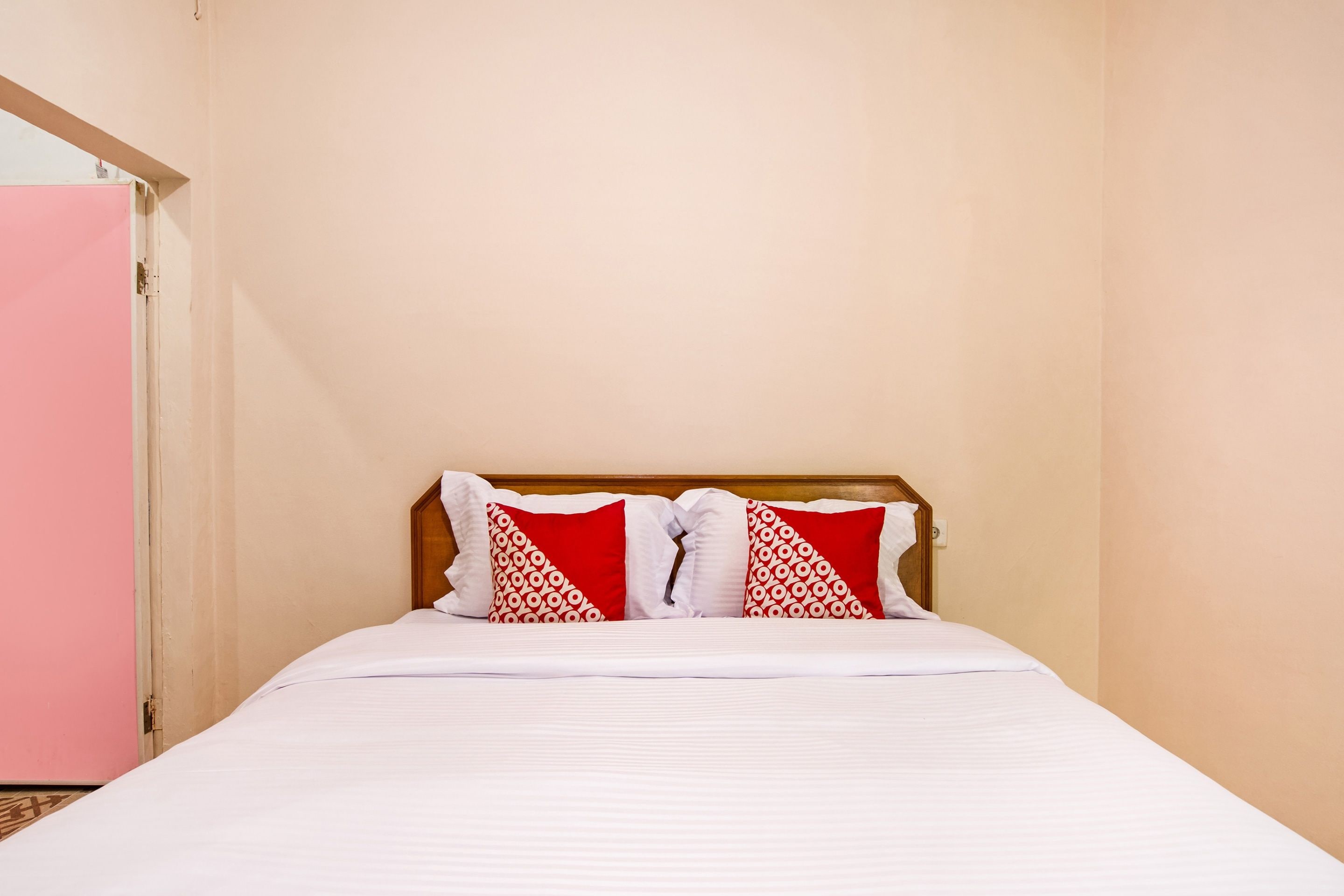 A single bed with a wooden headboard, white bedding, and two red pillows with white patterns.