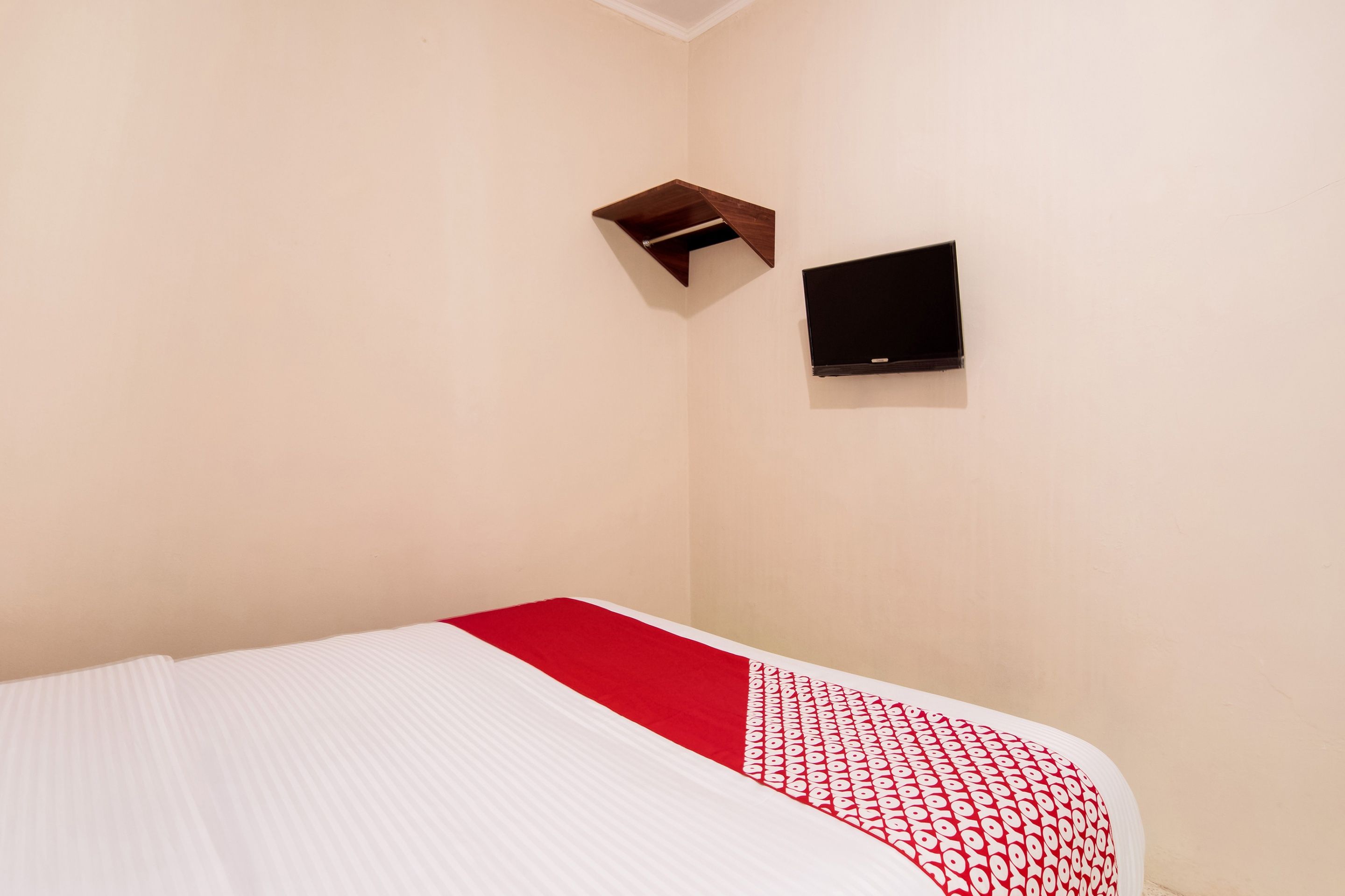 A room with a bed, a TV mounted on the wall, and a small wooden shelf.