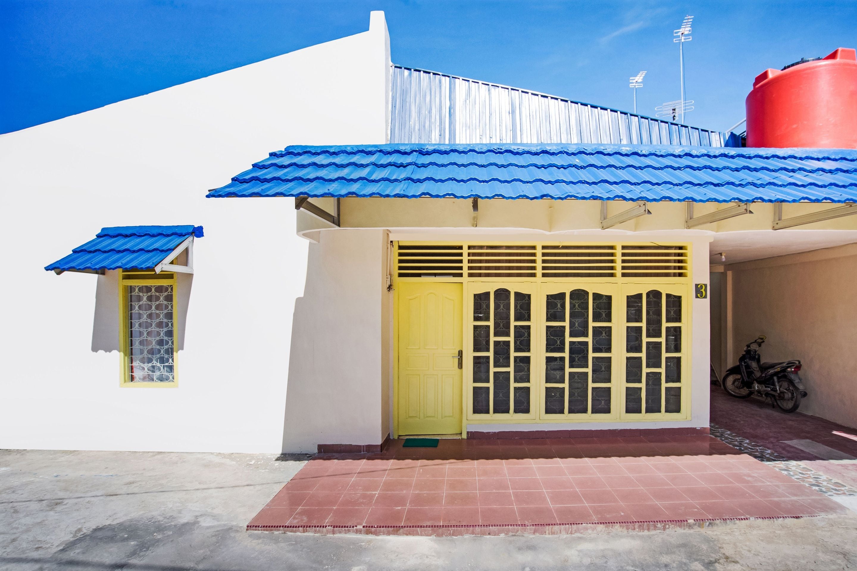 A building with a yellow door, a blue roof, and a red water tank.