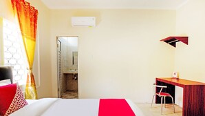 A hotel room with a bed, a desk, and a chair. There is a window with curtains, an air conditioning unit on the wall, and a door leading to a bathroom. - OYO 3252 Lansano Residence (Padang)