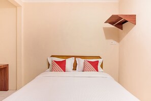A neatly made bed with white bedding and two red patterned pillows, a wooden headboard, and a small wooden shelf on the wall. - OYO 3252 Lansano Residence (Padang)