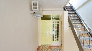 A staircase leading to a yellow door with a vent above it. - OYO 3252 Lansano Residence (Padang)