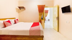 A neatly made bed with a red and white patterned bedspread, a mounted television on the wall, and a door leading to another room. - OYO 3252 Lansano Residence (Padang)