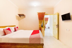 A neatly made bed with a red and white patterned bedspread, a mounted television on the wall, and a door leading to another room. - OYO 3252 Lansano Residence (Padang)