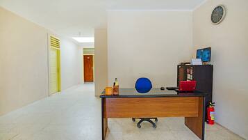 A hallway with a wooden desk, a blue chair, a red laptop, a fire extinguisher, and a clock on the wall.