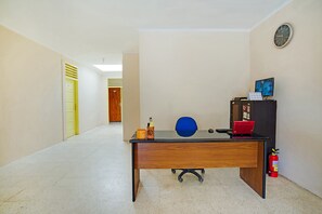 A hallway with a wooden desk, a blue chair, a red laptop, a fire extinguisher, and a clock on the wall. - OYO 3252 Lansano Residence (Padang)