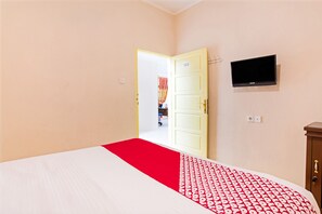 A hotel room with a bed, a television on the wall, and a door leading to another room. - OYO 3252 Lansano Residence (Padang)