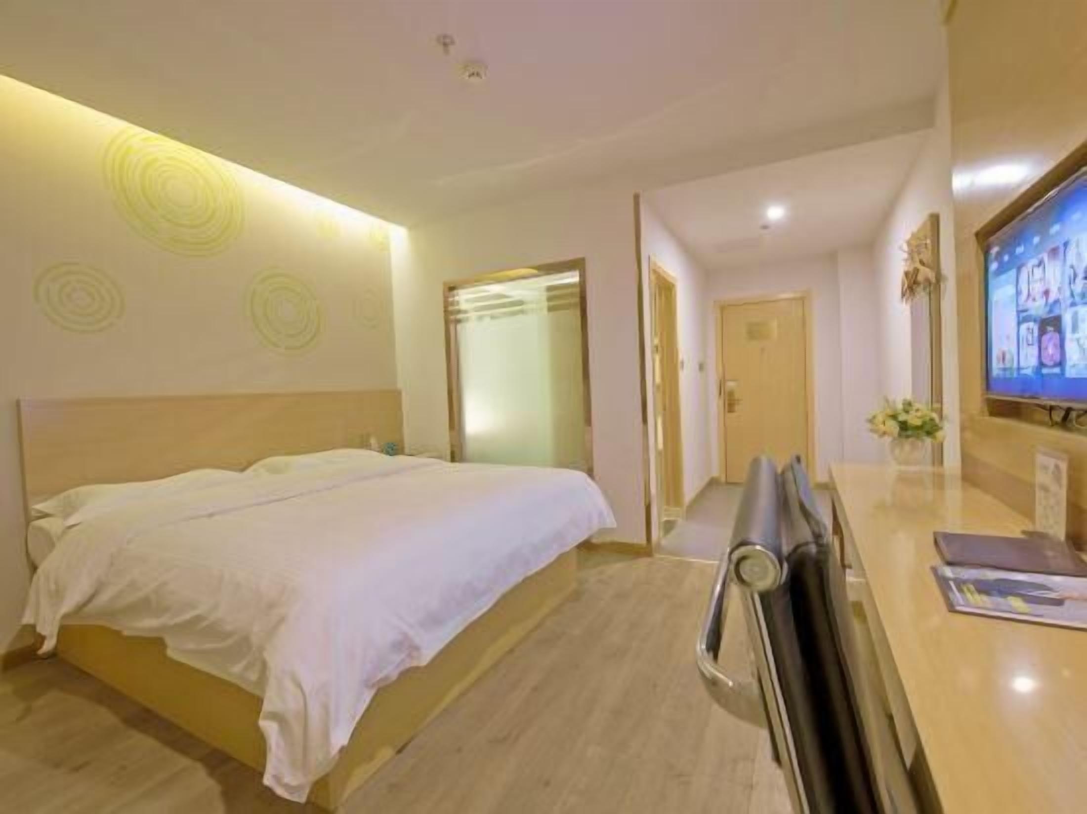 A hotel room with a bed, a desk with a chair, a television, and a door leading to another room.