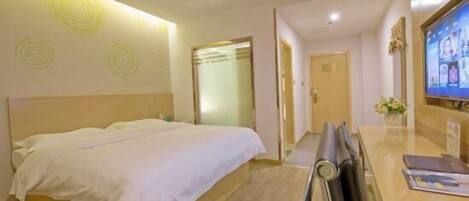 A hotel room with a bed, a desk with a chair, a television, and a door leading to another room.