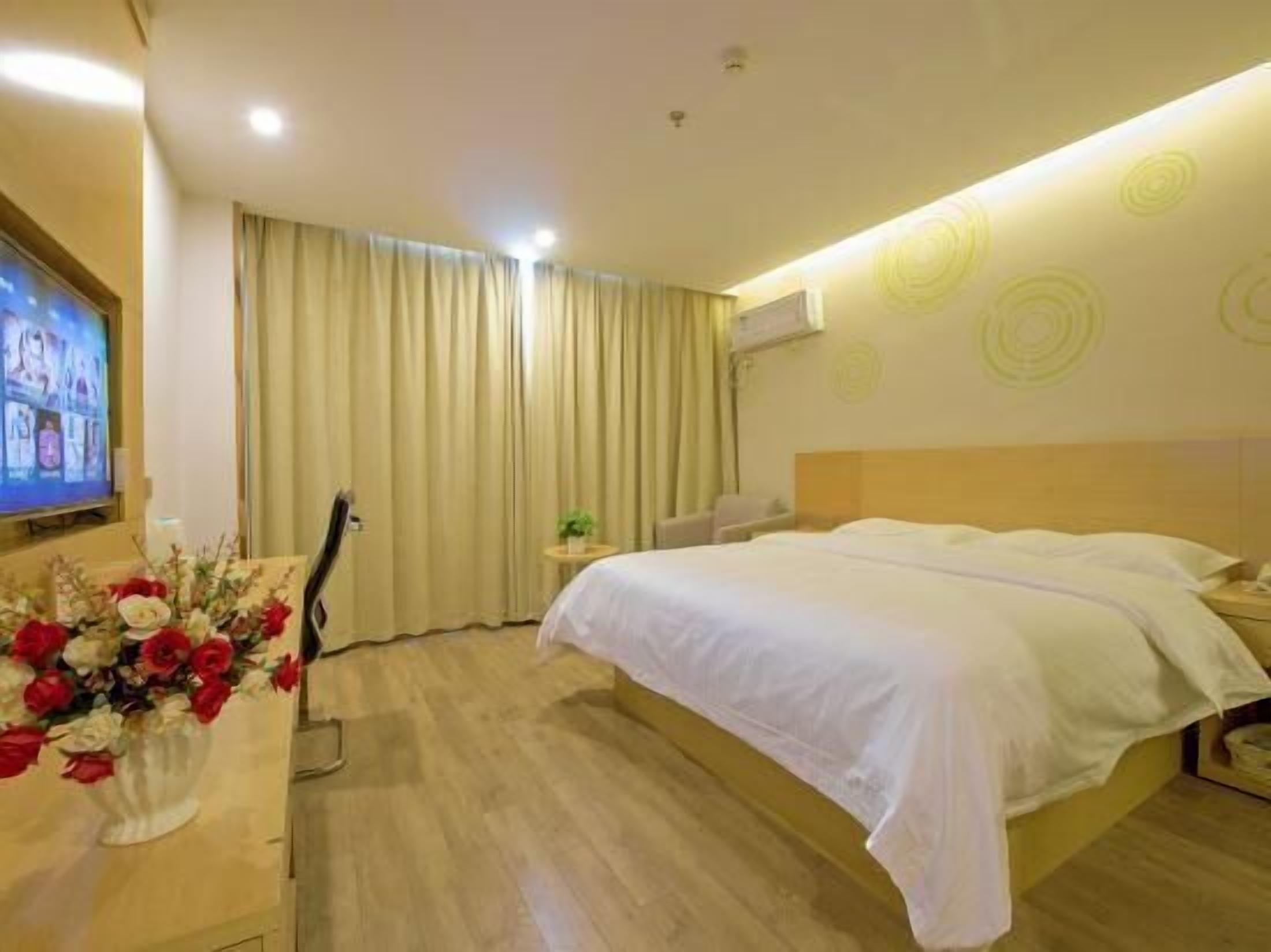 Ein Hotelzimmer mit Bett, Fernseher, Schreibtisch mit Blumenvase und Fenster mit Vorhängen.