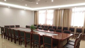 A conference room with a long table and chairs, a potted plant, and large windows with curtains.