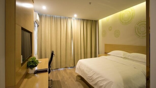 A modern hotel room with a bed, a desk, a chair, and a TV.
