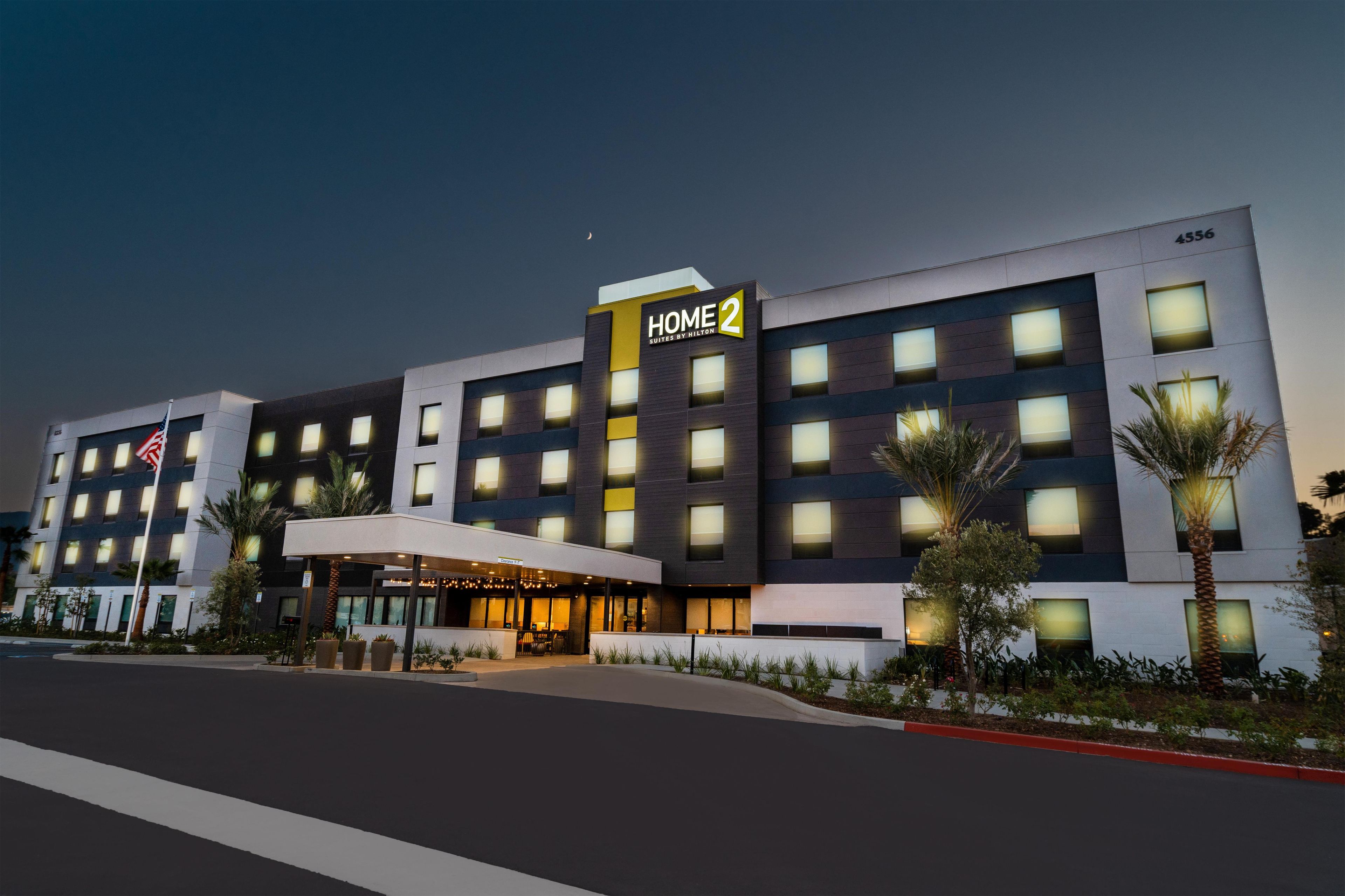 A multi-story hotel with a prominent 'HOME 2' sign, a covered entrance, and a flagpole with an American flag.