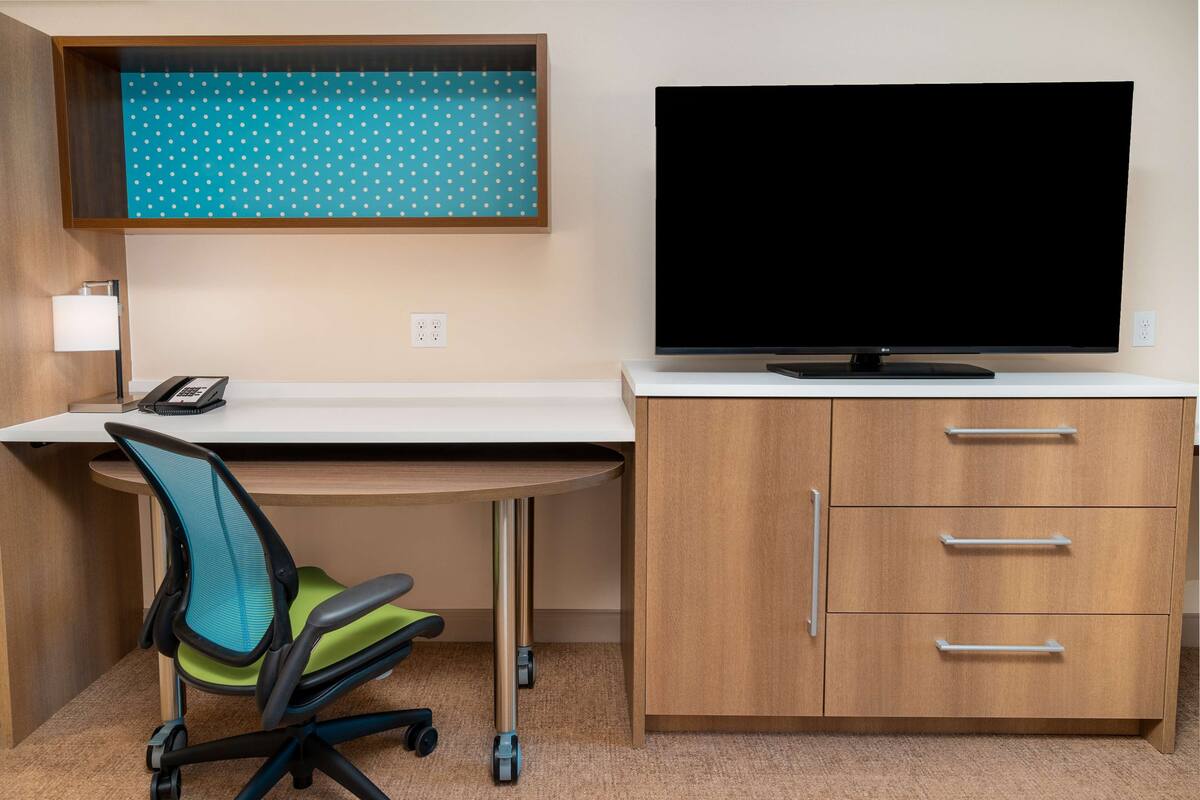 A hotel room with a desk, a chair, a television, and a cabinet.