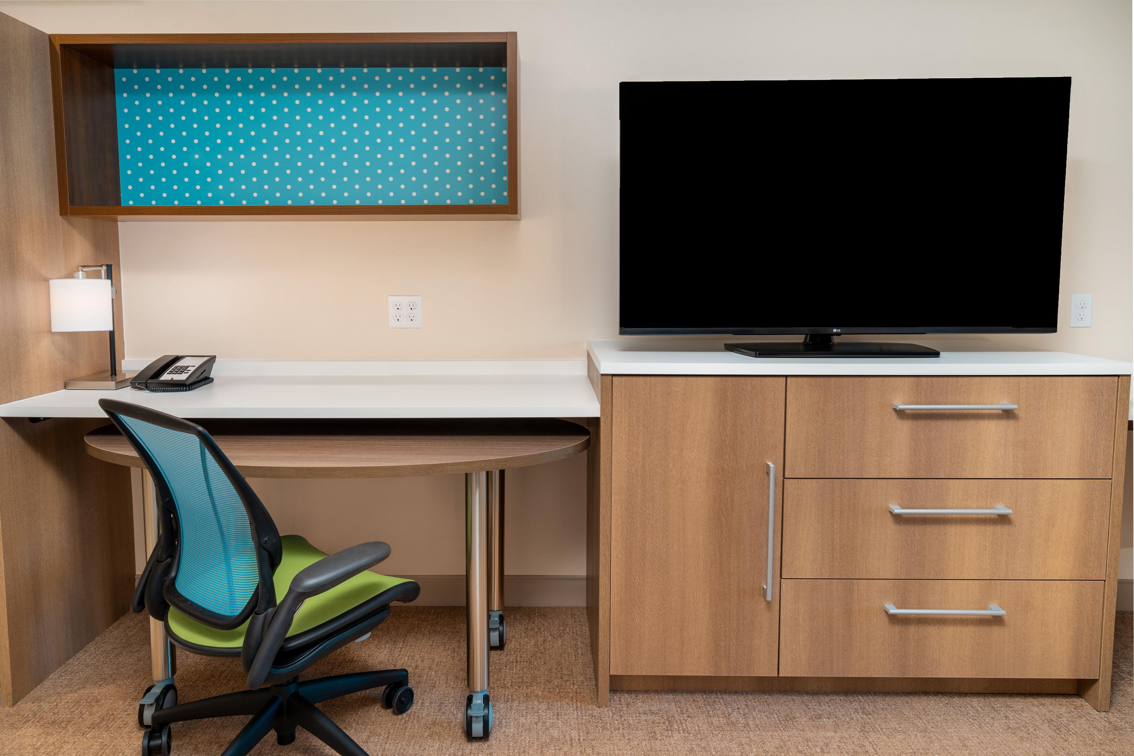 A modern office space with a desk, chair, TV, and storage cabinet.