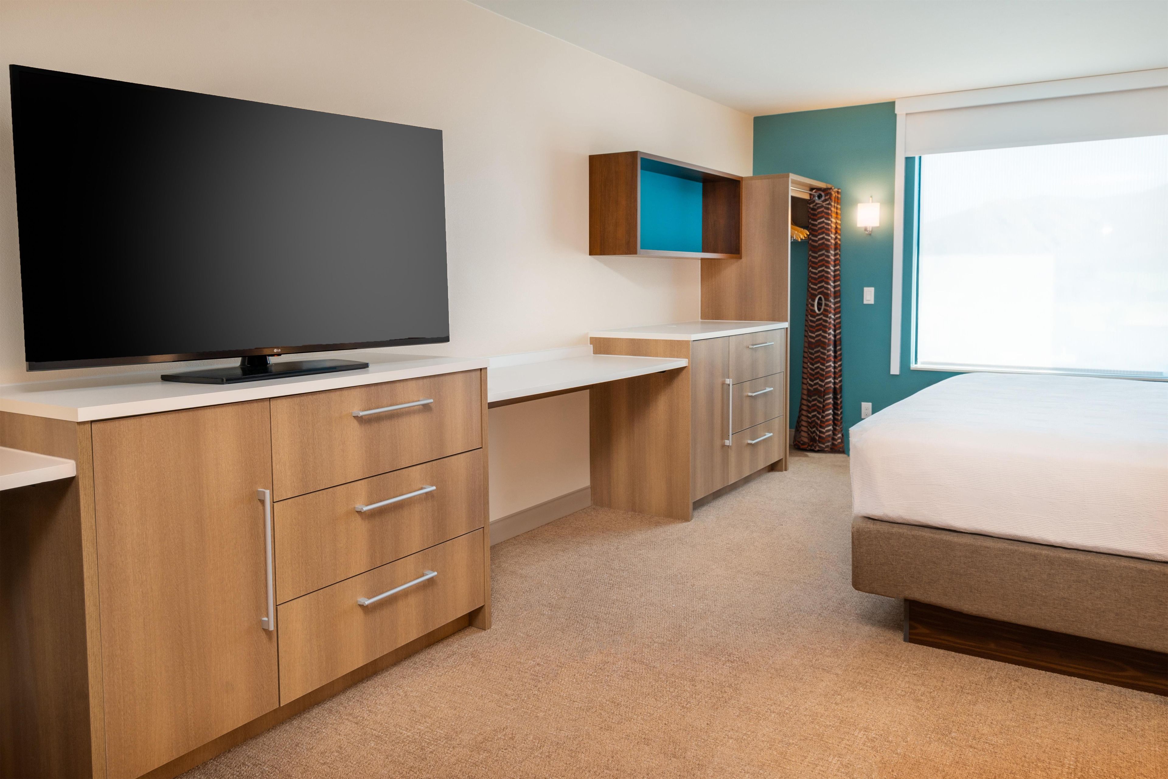 A modern hotel room with a flat-screen TV, wooden furniture, a bed, and a window.