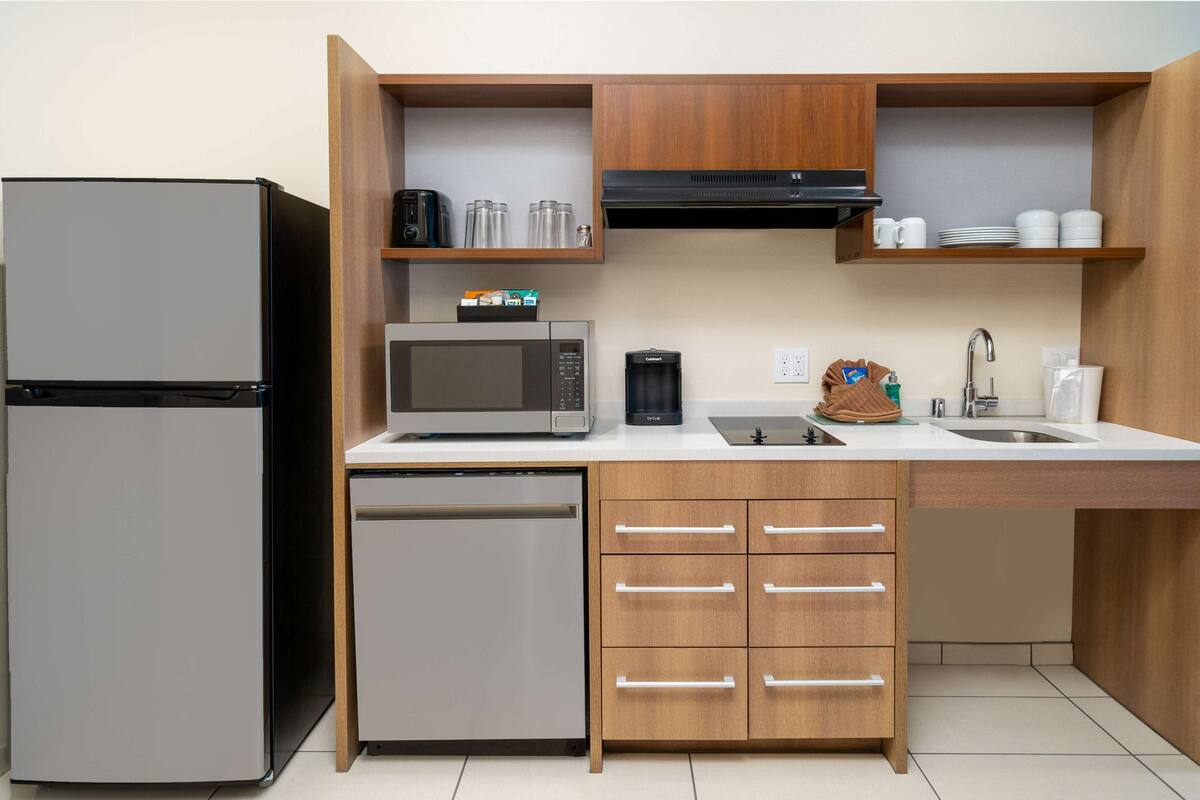A compact kitchen with a refrigerator, microwave, coffee maker, and a dishwasher.