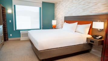 Une chambre d’hôtel avec un grand lit, une fenêtre avec des rideaux, une lampe fixée au mur et un thermostat.