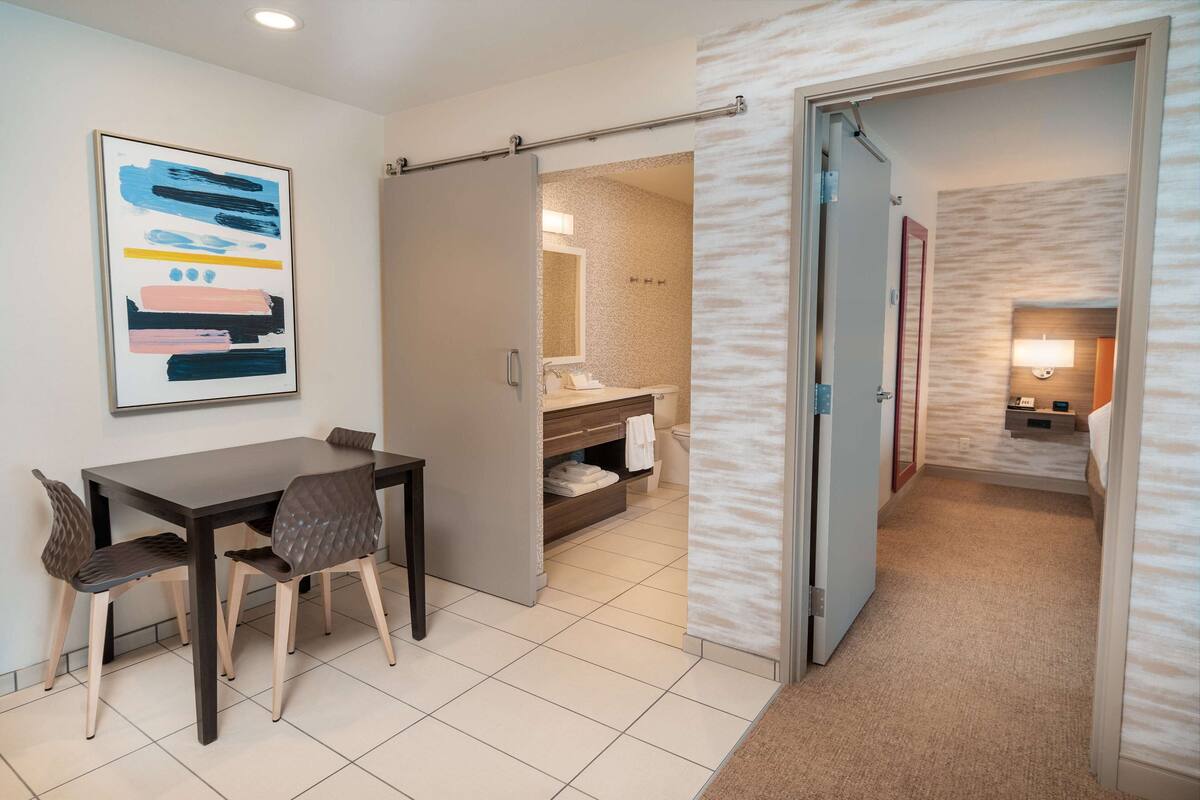 A hotel room with a dining area, a bathroom, and a hallway.
