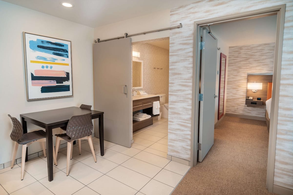 A hotel room with a dining area, a bathroom, and a hallway.