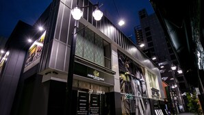 A modern hotel with a prominent entrance, large windows, and a well-lit facade. - Design Hotel Blax (Hachioji)