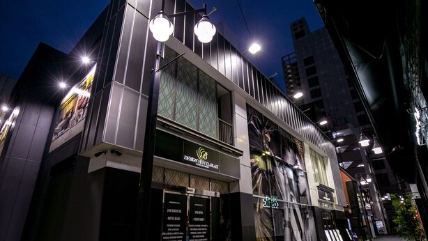A modern hotel with a prominent entrance, large windows, and a well-lit facade. - Design Hotel Blax (Hachioji)
