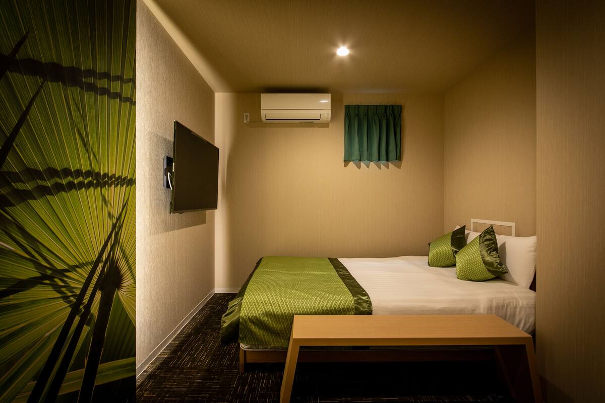 Ein Hotelzimmer mit einem Bett, einem Nachttisch, einem an der Wand befestigten Fernseher und einer Klimaanlage.