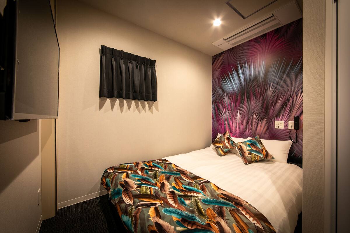 Ein Hotelzimmer mit Bett, Wandfernseher, Vorhang und einem farbenfrohen Wandgemälde.