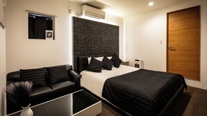 A modern hotel room with a bed, a sofa, a small table, and a nightstand. - Design Hotel Blax (Hachioji)