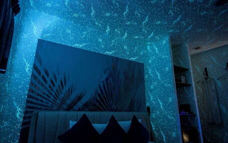 A room with a bed, a large abstract painting, and a starry ceiling effect.