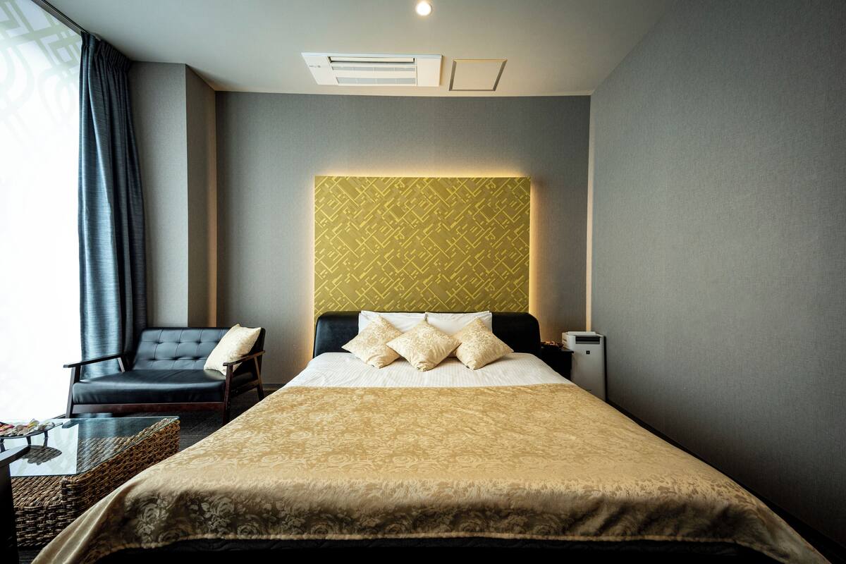 Ein Hotelzimmer mit Bett, Sessel, Nachttisch und Wandklimaanlage.