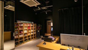 A modern hotel reception area with a wooden reception desk, a large bookshelf filled with toiletries, and a digital display screen. - Design Hotel Blax (Hachioji)