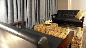 A living room with a black leather sofa, a wicker coffee table, and a black armchair. - Design Hotel Blax (Hachioji)